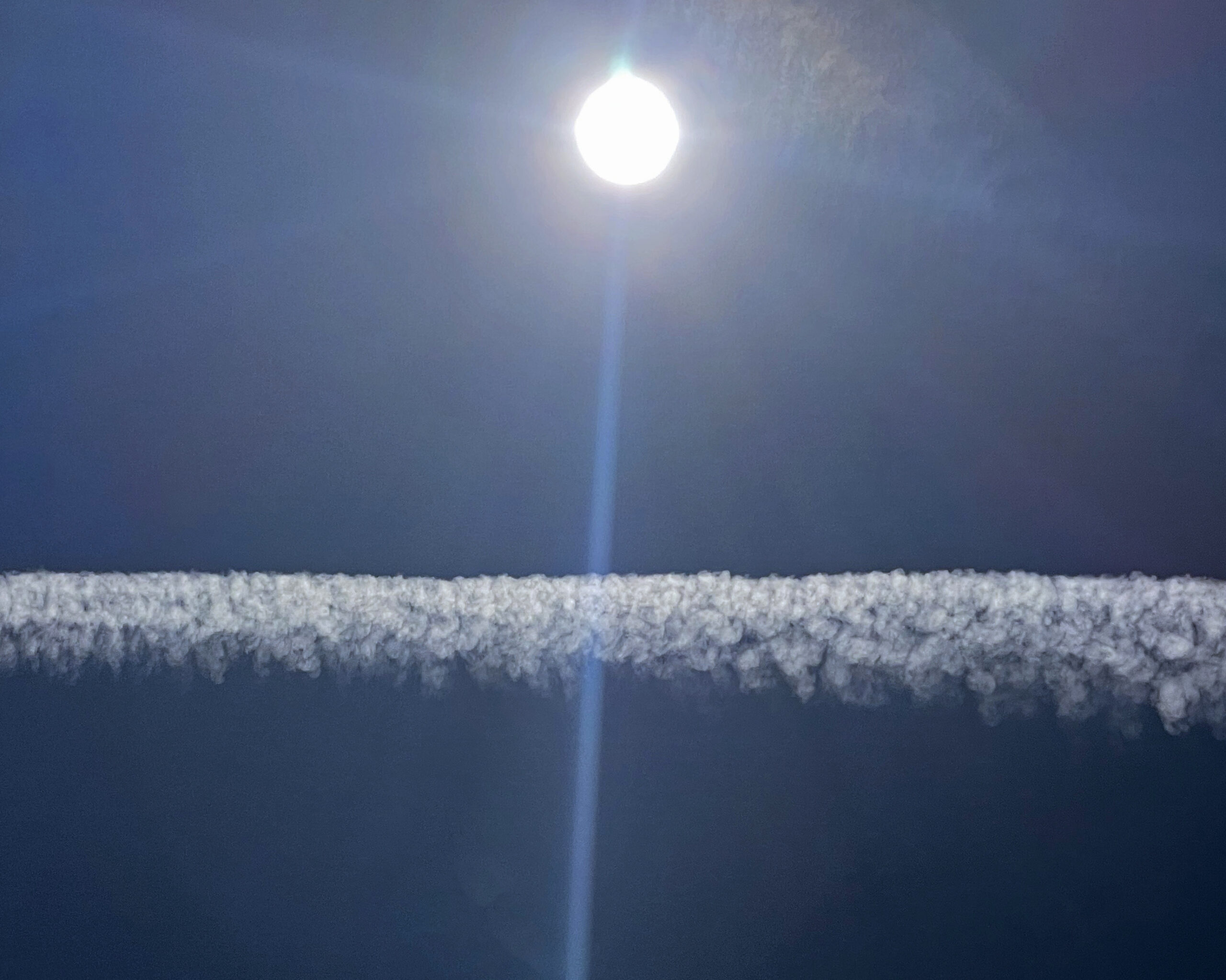 Image of the sun flaring light over an airplane contrail.