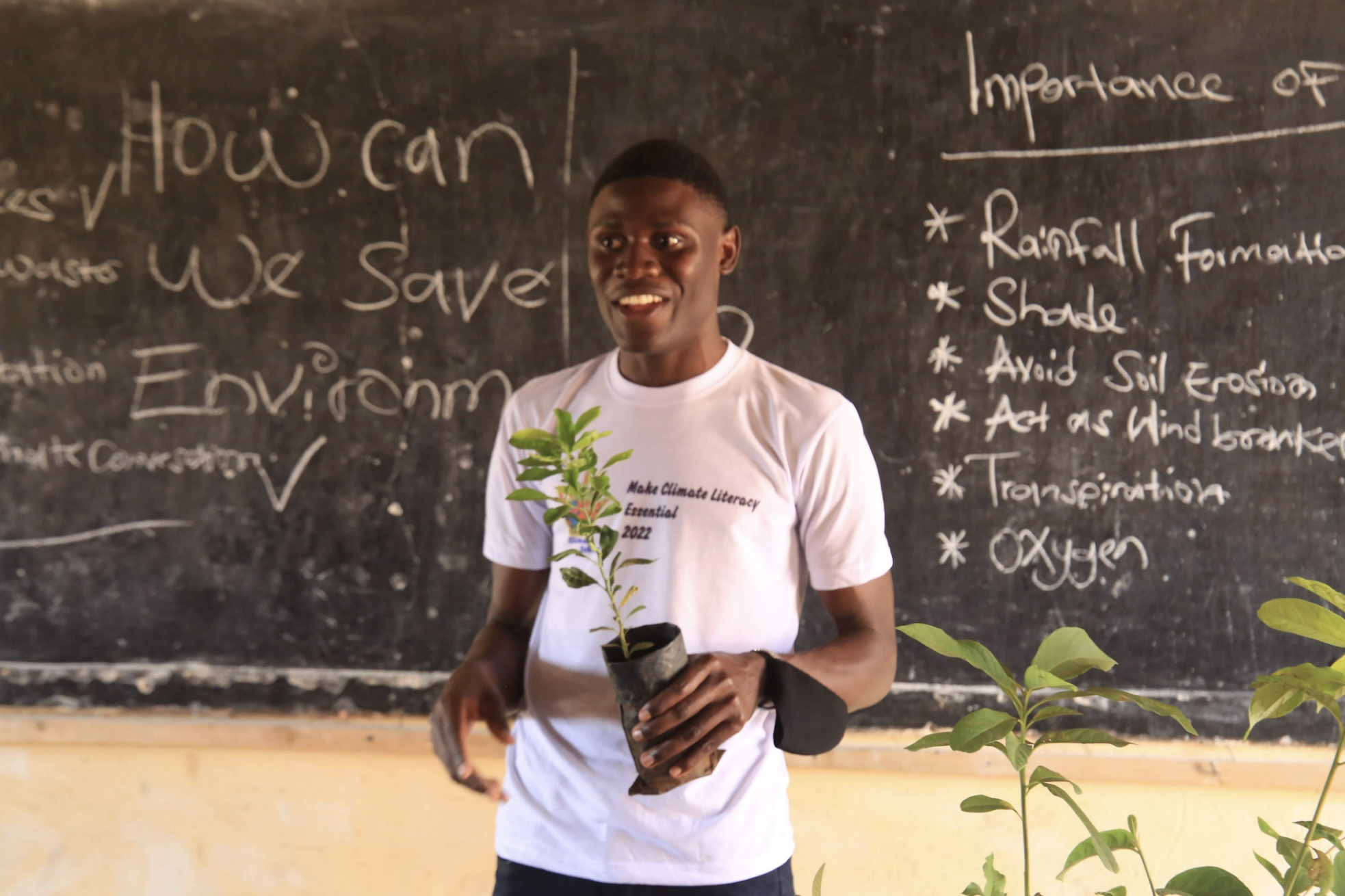 Nyombi Morris smiling in front of a chalkboard that reads "how can we save the environment"