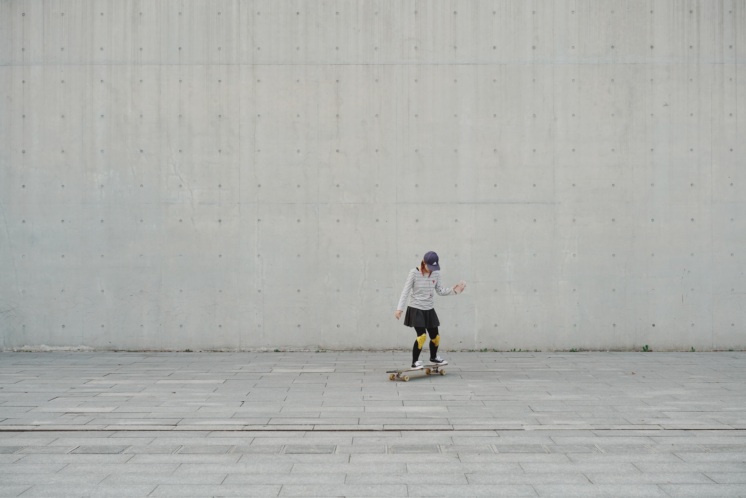 A child skateboards on concrete ground, with a concrete wall in the background