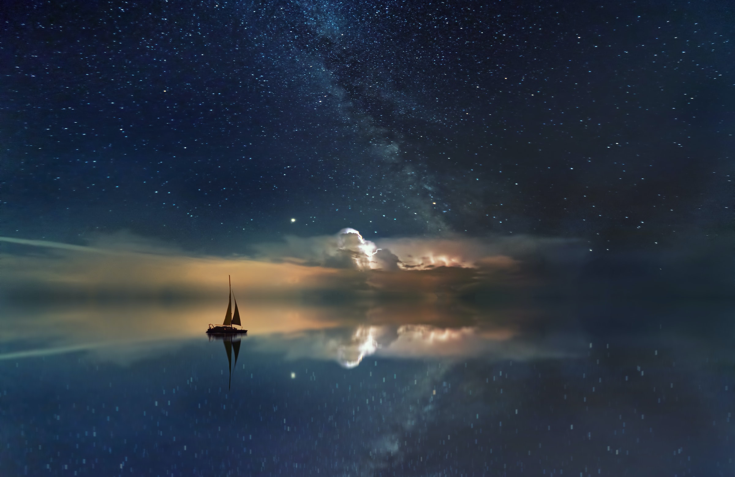 A night sky over water with a sailboat
