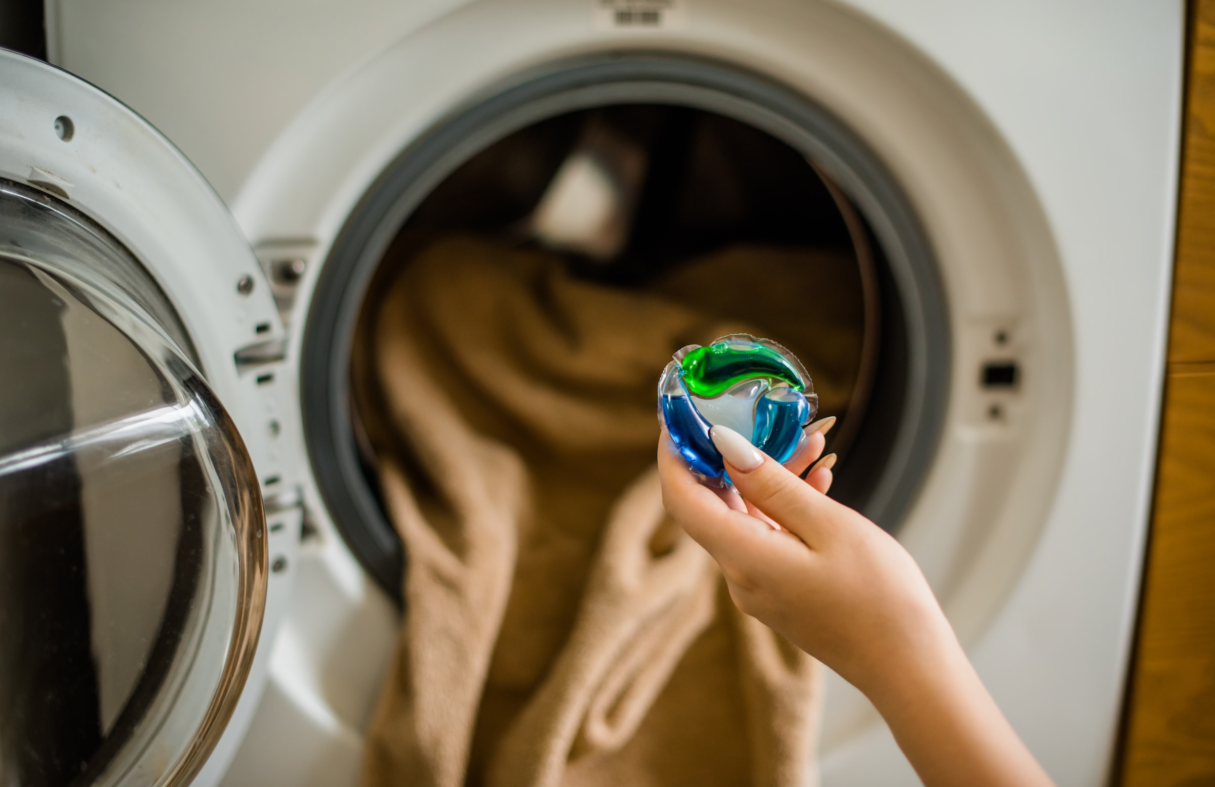 A laundry detergent pod is held up in front of a laundry machine