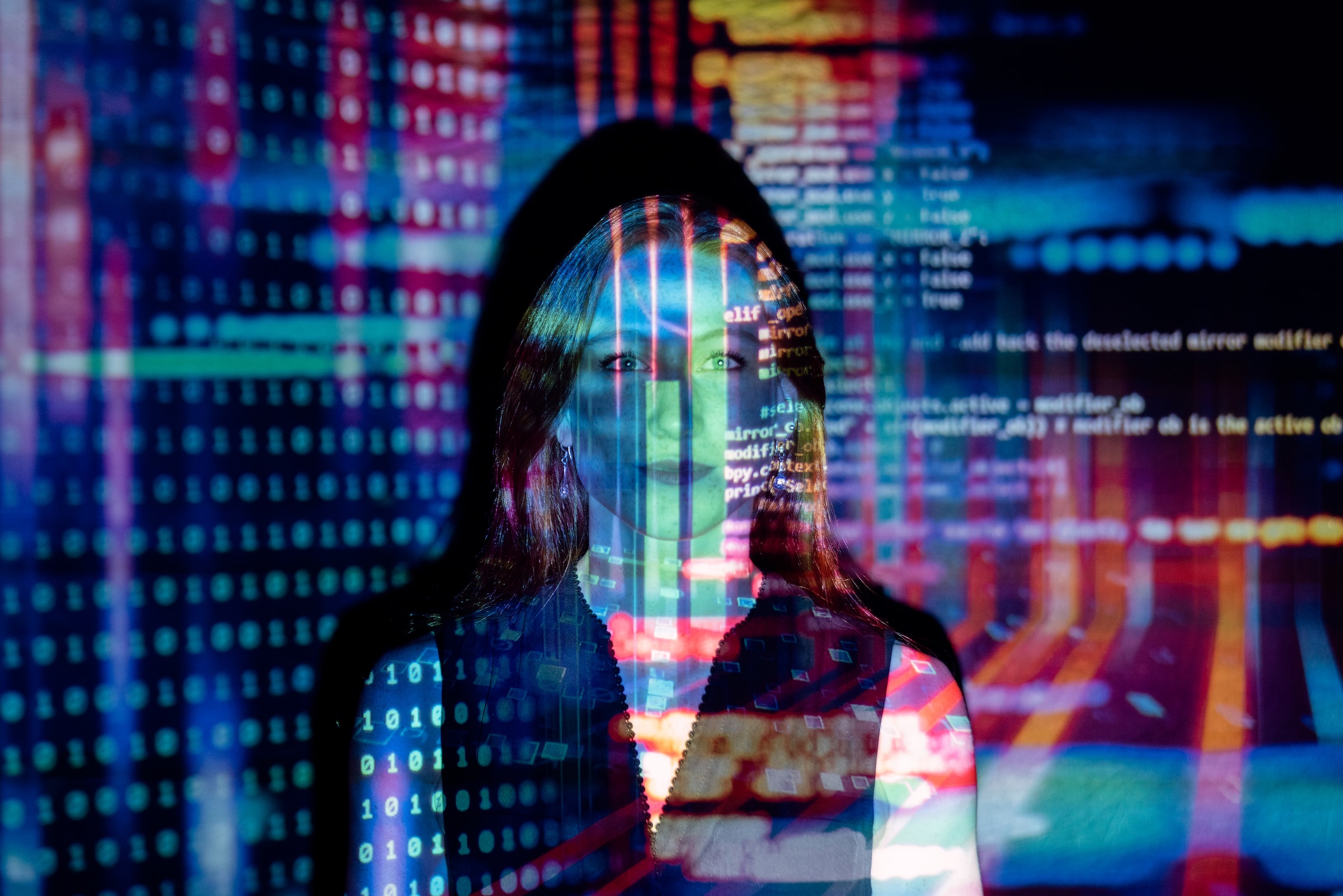 Computer code and various color patterns are projected onto a woman's face