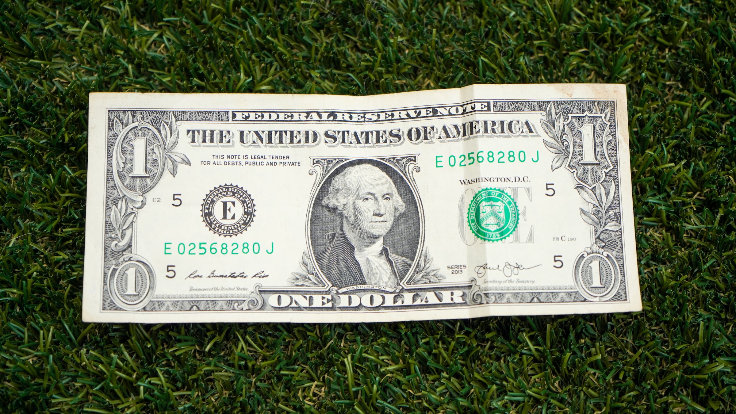 A one-dollar bill is displayed against a grass background