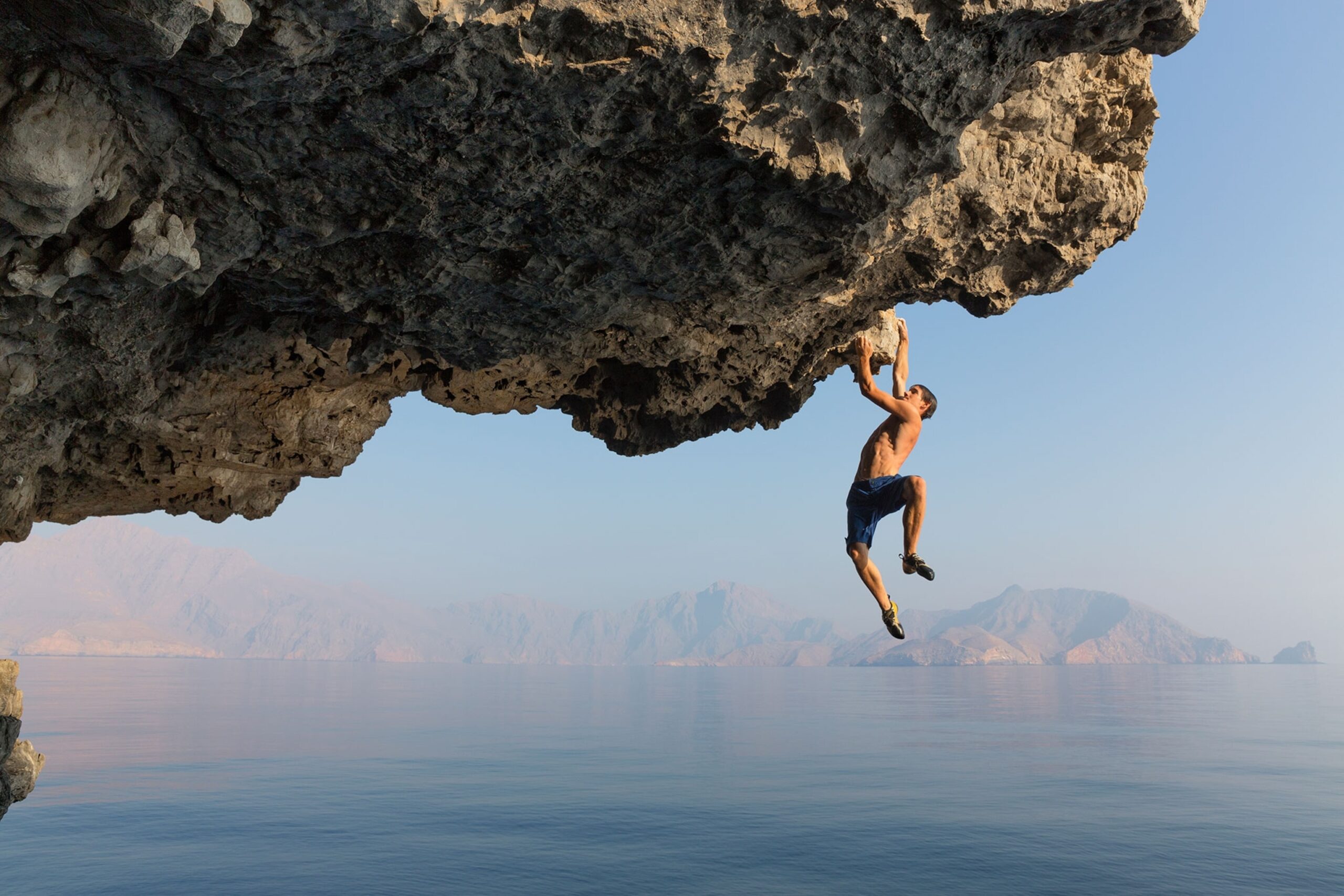 Alex Honnold rock climbing on a steep overhang over the ocean