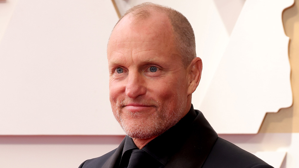Woody Harrelson smiling in front of a white and beige wall