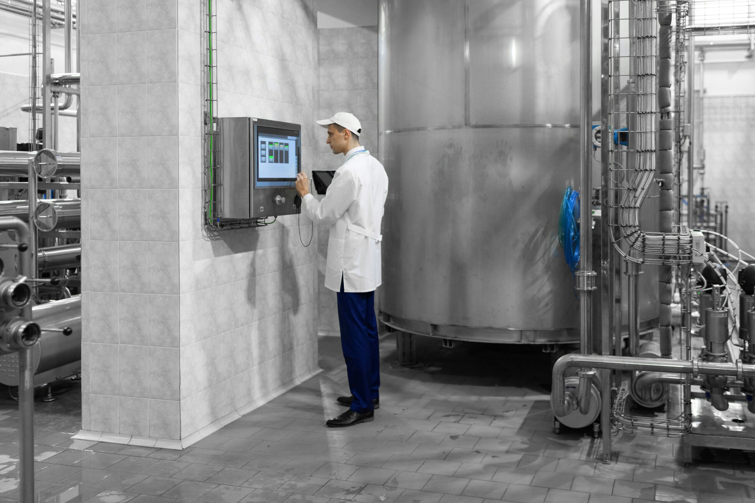 Worker in white lab coat using a digital screen on a metal box in an industrial room of equiptment.