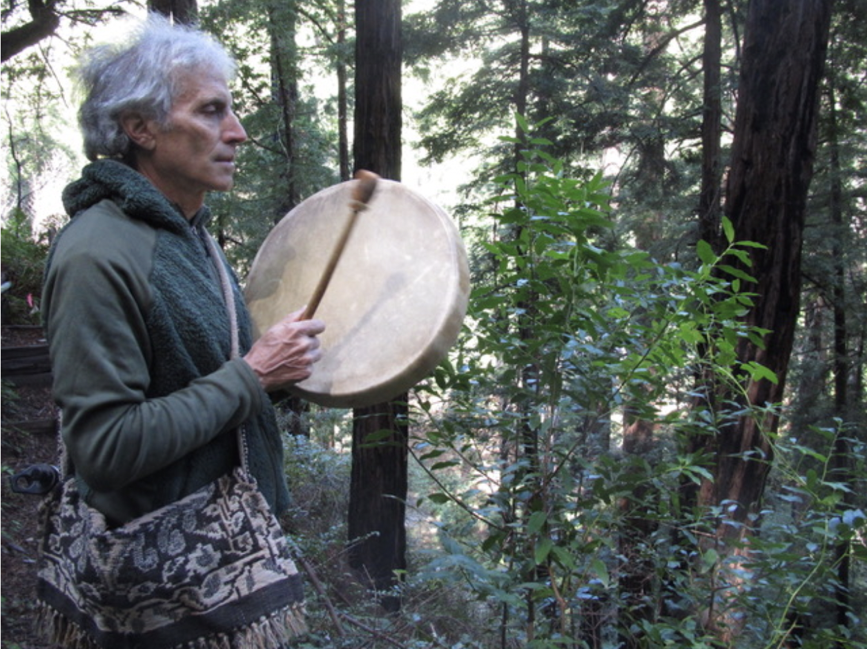 Bill Plotkin playing a hand drum in a forest setting